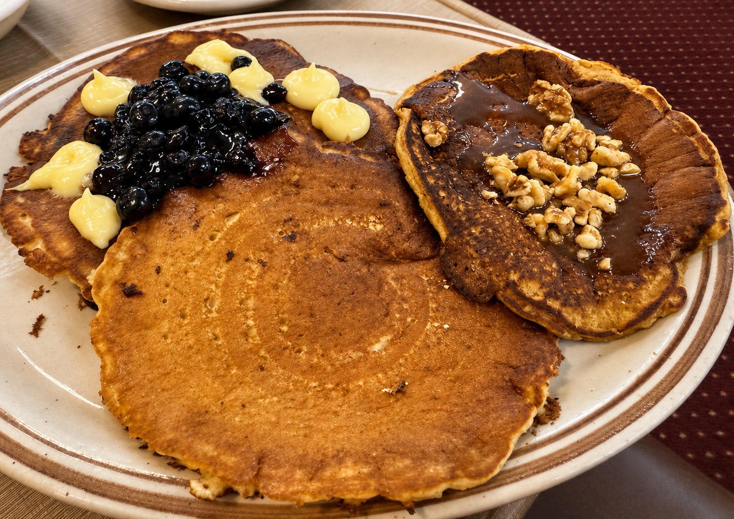 A tall stack of pancakes topped with blueberries, blackberries and walnuts